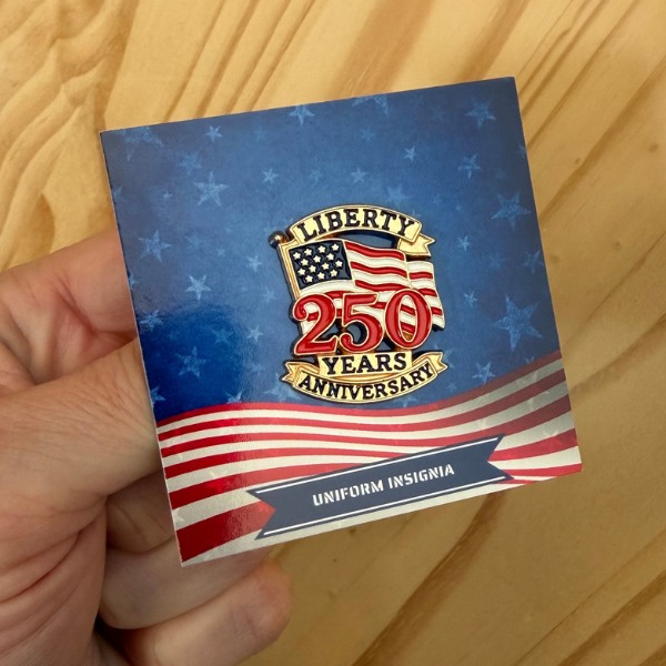 250-years-anniversary-pin2 - Agent Gear USA Blue box with a Liberty 250 Years Anniversary emblem over a waving US flag background, labeled 'Uniform Insignia', held in a hand.