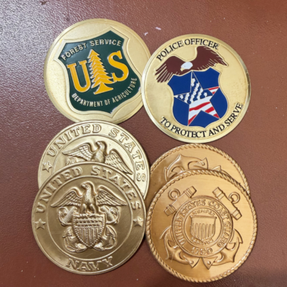 Collection of five commemorative coins featuring government agency emblems: Forest Service (US), Police Officer shield, US Navy eagle seals, and Coast Guard insignia on copper and gold-toned medals.