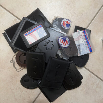 Pile of black leather card holders, pouches, and small wallets scattered on beige tiled floor, some with US flag patches on them.
