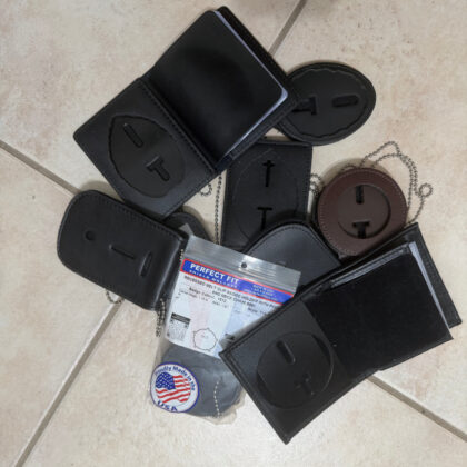 Assortment of black leather belt loops and clips with metal chains scattered on a beige tiled floor, including a small Perfect Fit package and a round USA badge.